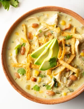 Top down view bowl of green chicken enchilada soup, topped with tortilla strips and slices of avocado.