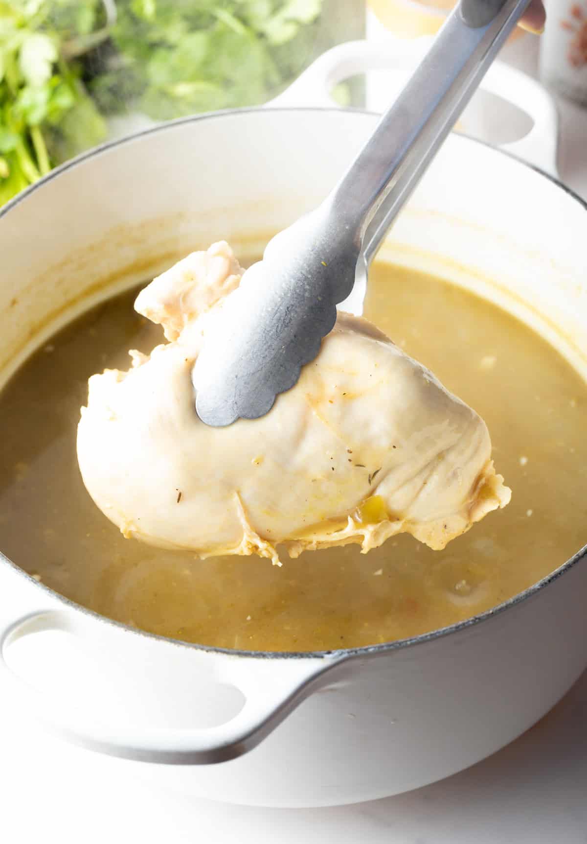 Tongs holding a cooked chicken breast over the pot.