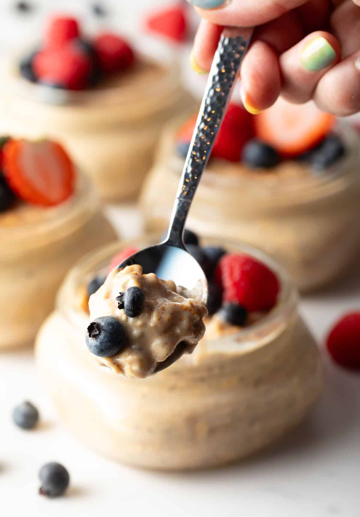 A spoon holding a bite of high protein oatmeal above a glass jar.