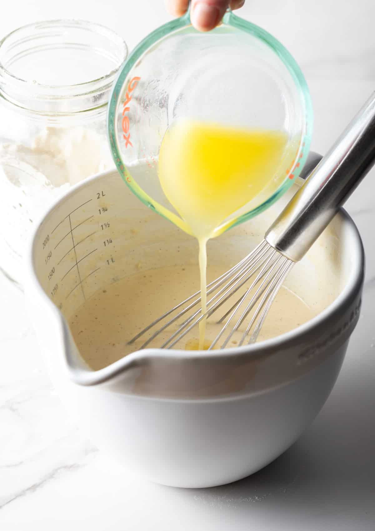 Melted butter is being added to a mixing bowl filled with a homemade pancake mix recipe.