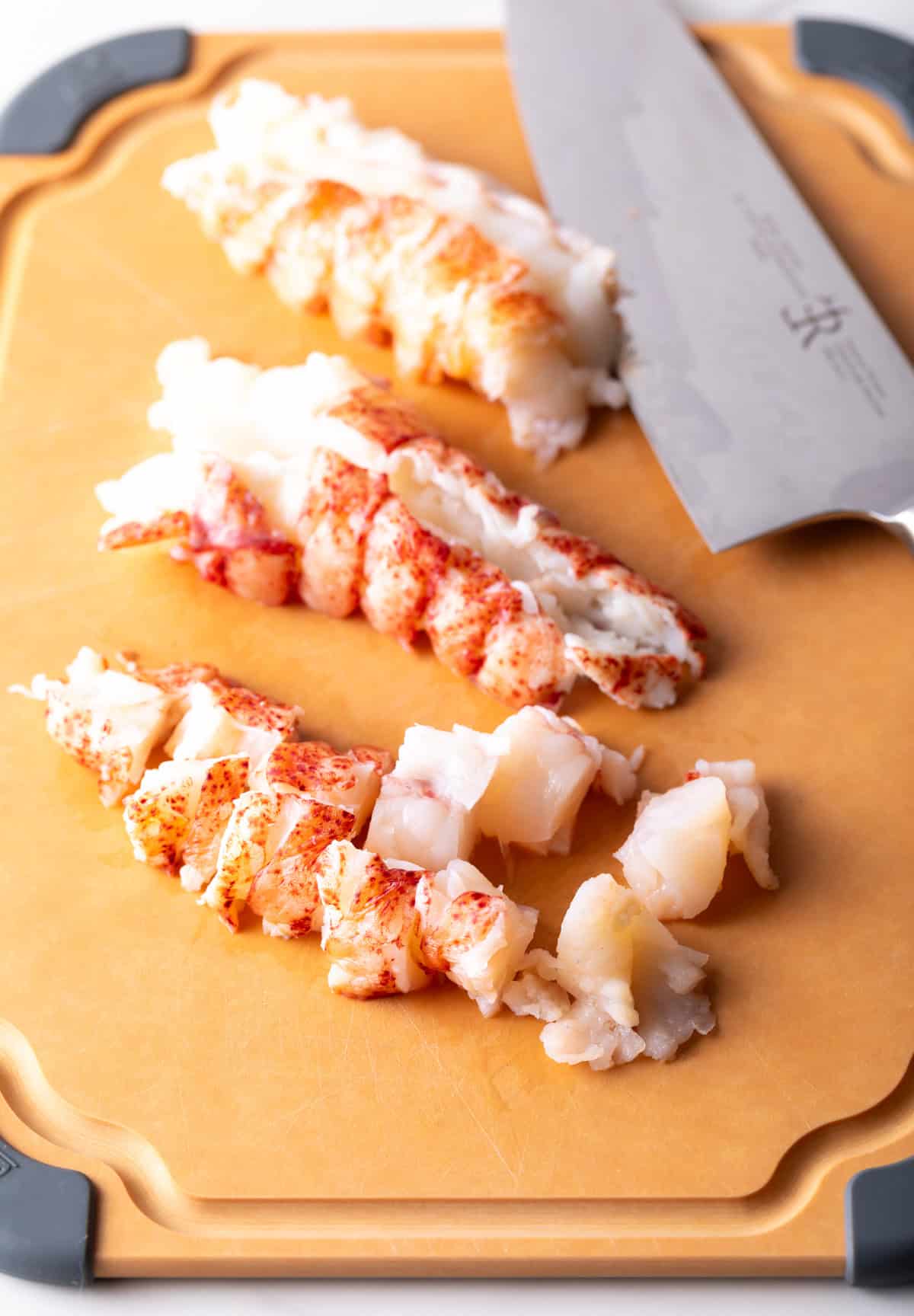 Cooked lobster on a cutting board that is chopped into bite sized pieces for lobster mac and cheese.