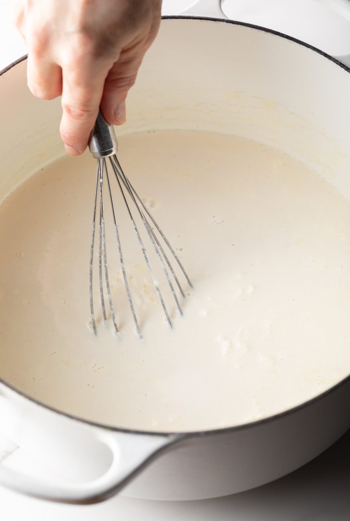 A whisk is whisking the roux and cream mixture for a lobster macaroni and cheese recipe.