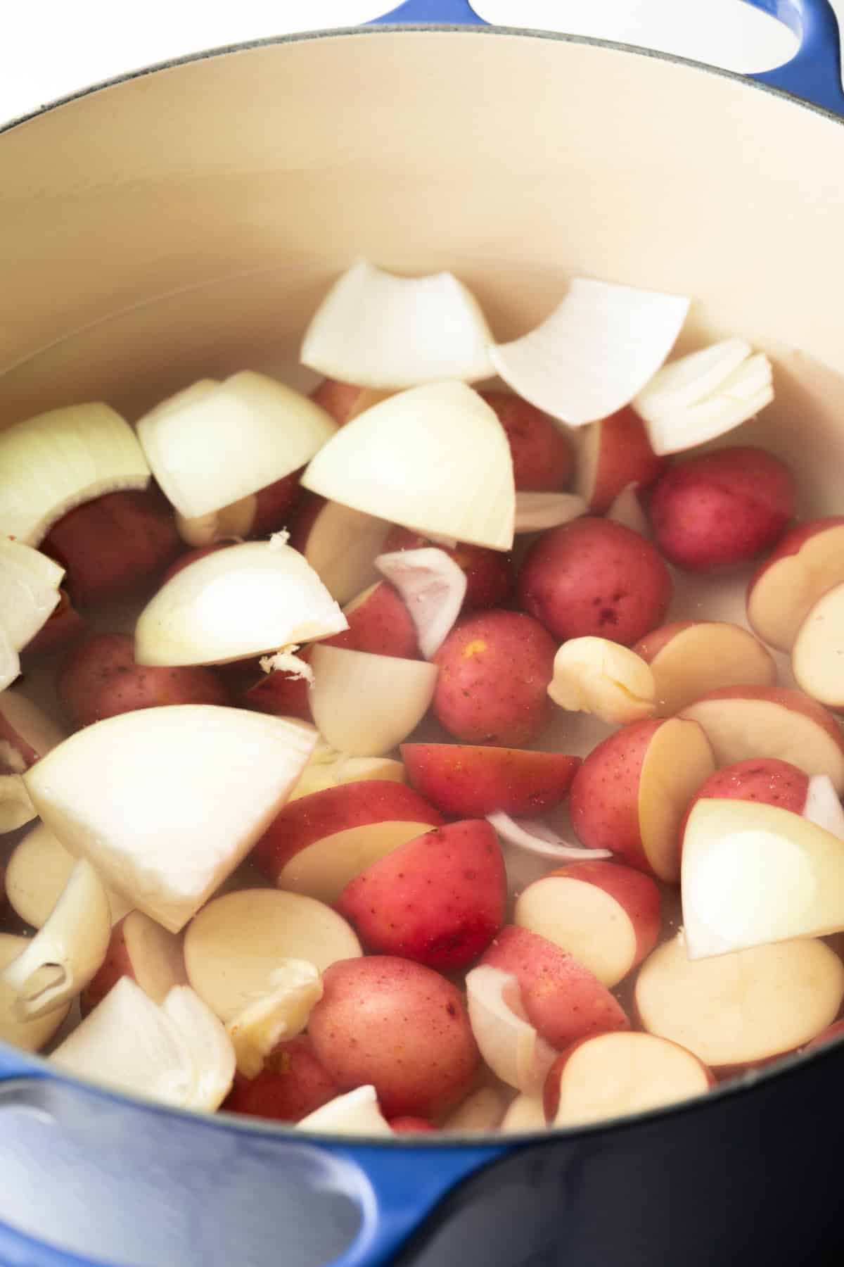 A pot filled with water, onion wedges, and baby red potatoes.