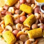 Overhead shot of a low country boil featuring shrimp, sausage, potatoes, and corn, with ramekins of dipping sauces on the side.