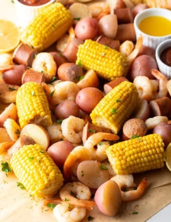 Overhead shot of a low country boil featuring shrimp, sausage, potatoes, and corn, with ramekins of dipping sauces on the side.