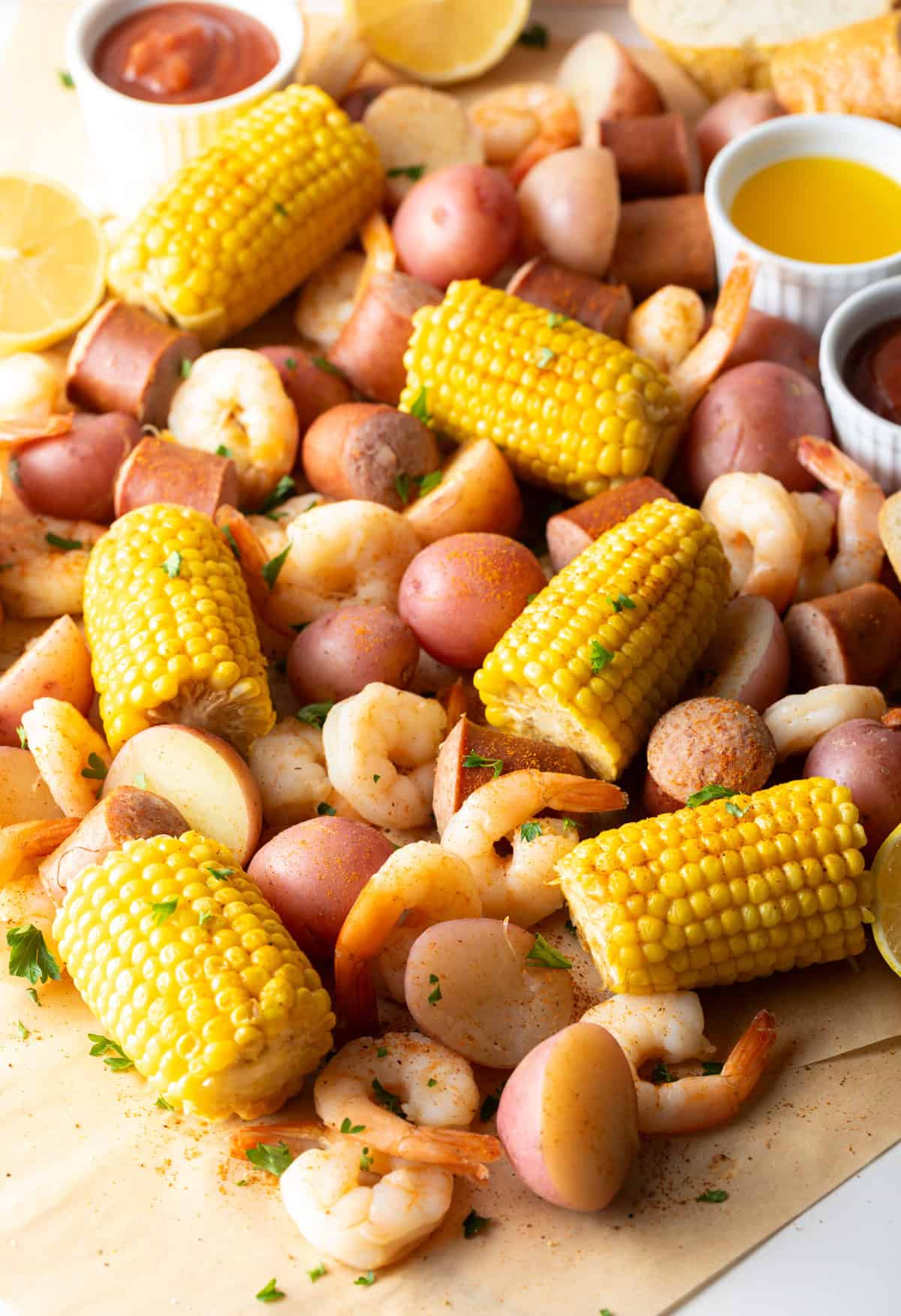 Overhead shot of a low country boil featuring shrimp, sausage, potatoes, and corn, with ramekins of dipping sauces on the side.