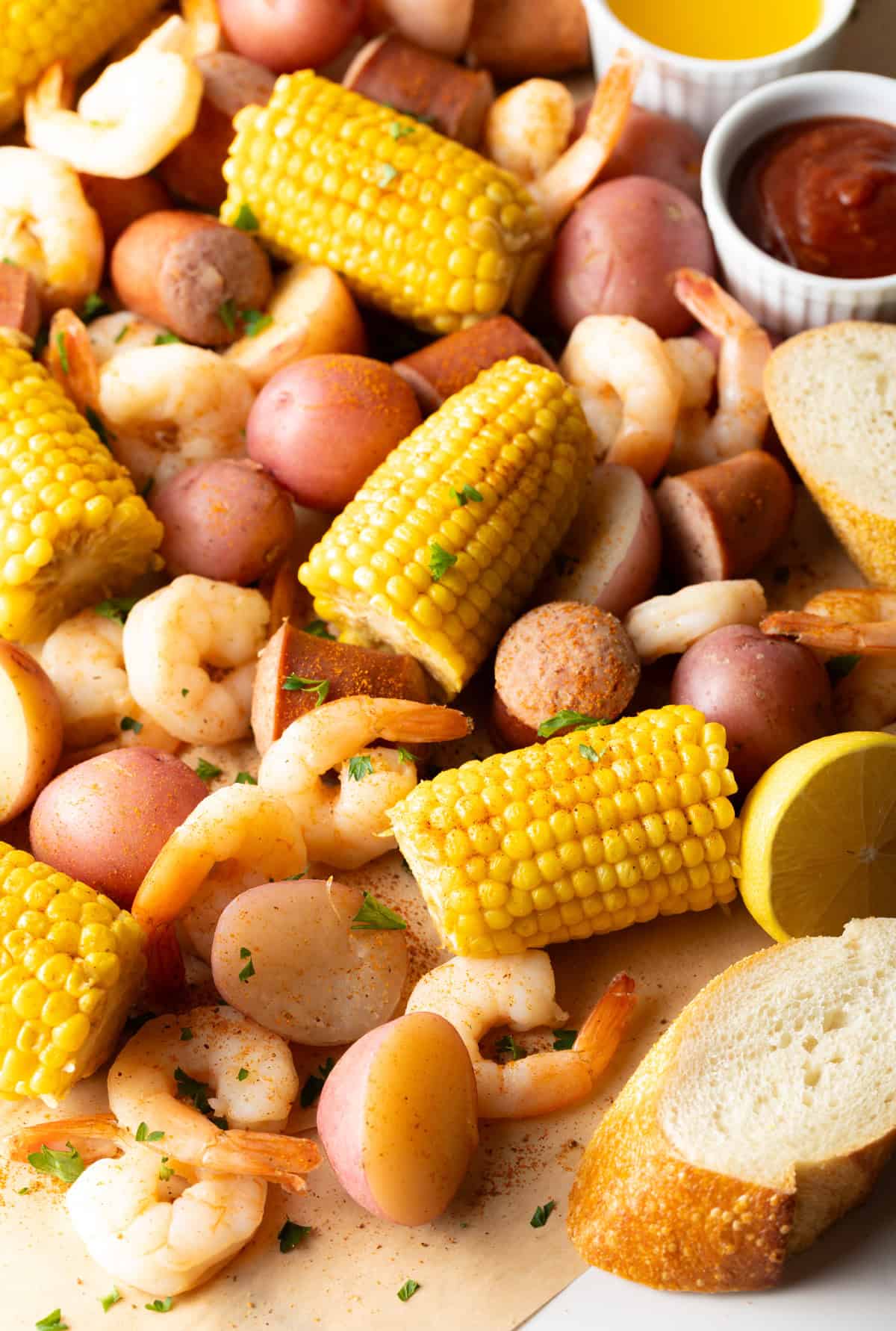 A platter full of boiled red potatoes, half pieces of corn on the cob, shrimp, and chunks of sausage, with slices of bread on the outside.