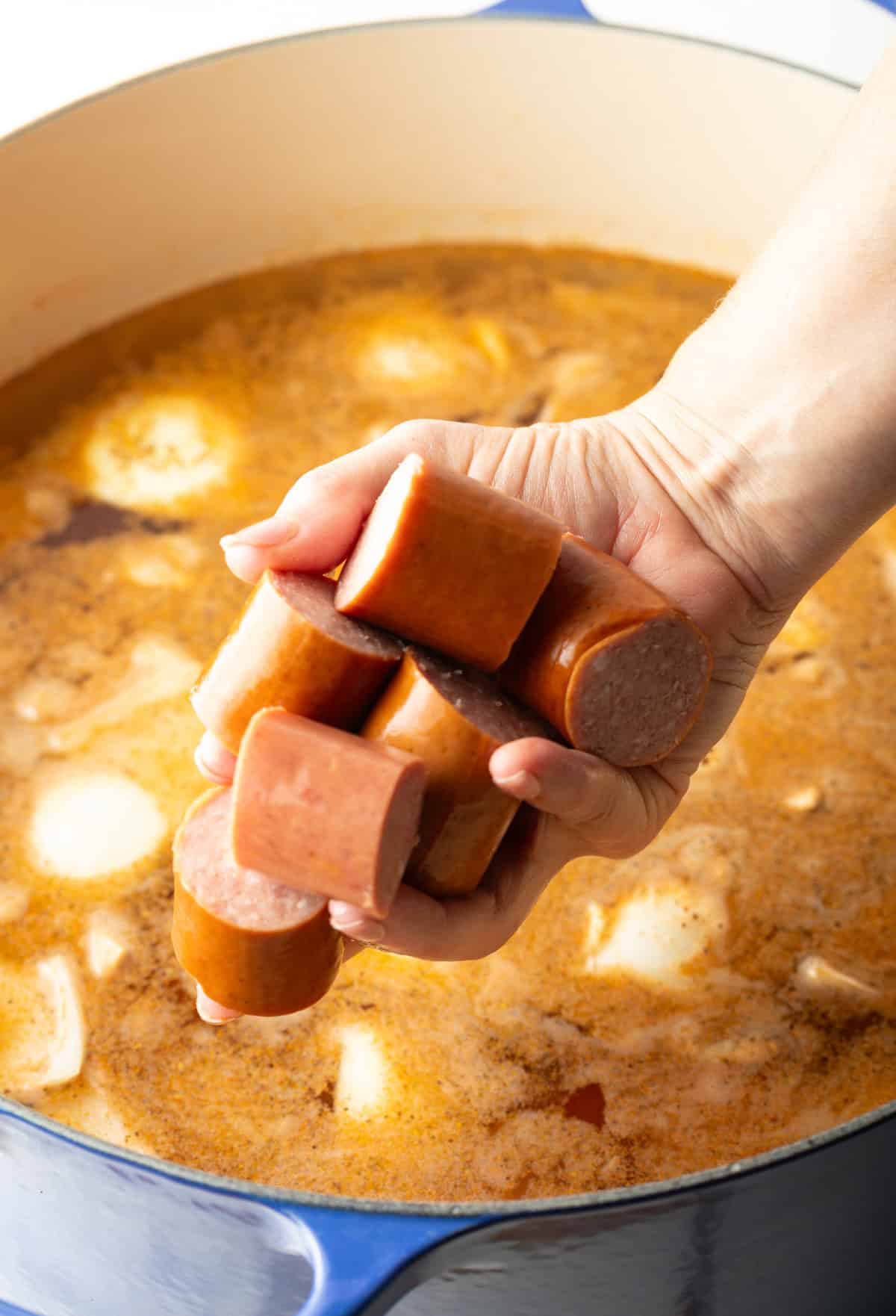 A hand holding kielbasa sausage that is being added to a pot of low country boil recipe.