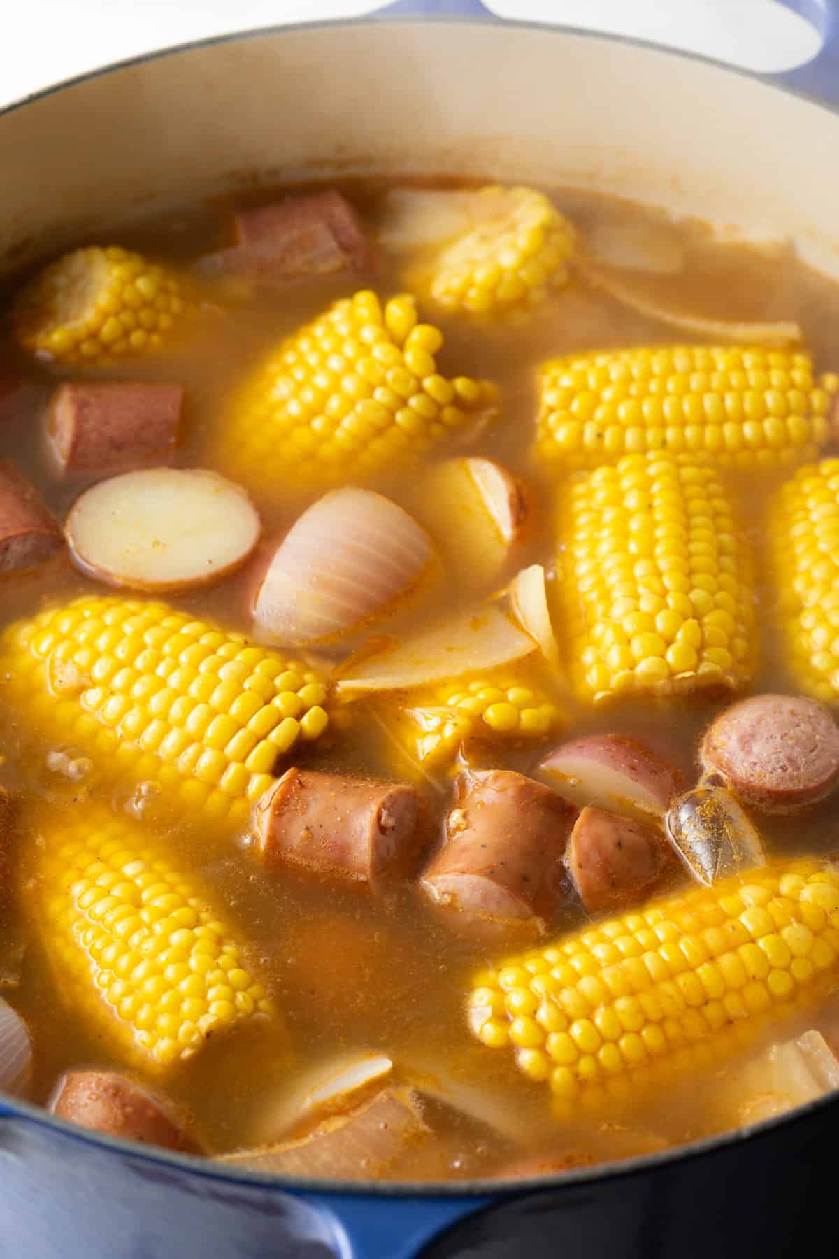 A pot of Old Bay seasoning spiced broth with corn, potatoes, onions, and sausage.