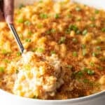 A spoon is scooping a serving of New Orleans style macaroni and cheese from a white dish.