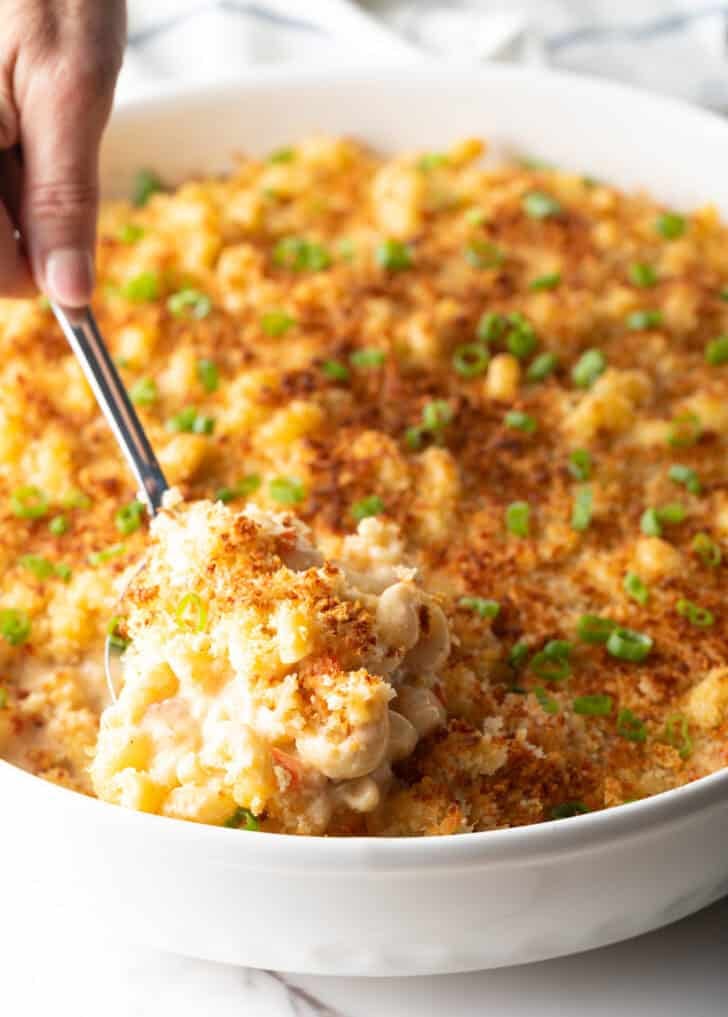 A spoon is scooping a serving of New Orleans style macaroni and cheese from a white dish.