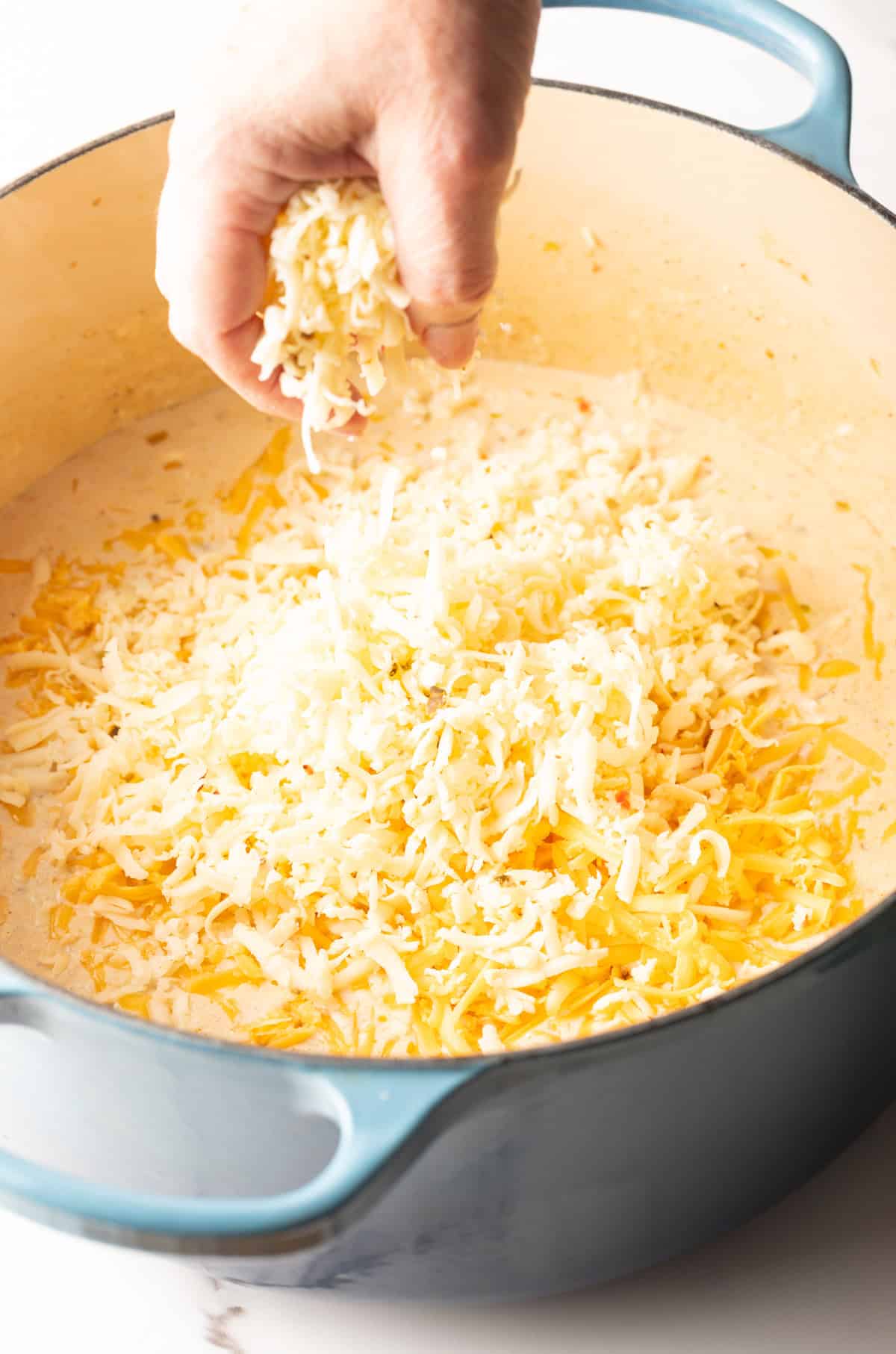 Grated cheese is being added to the cream mixture for Cajun style mac and cheese.
