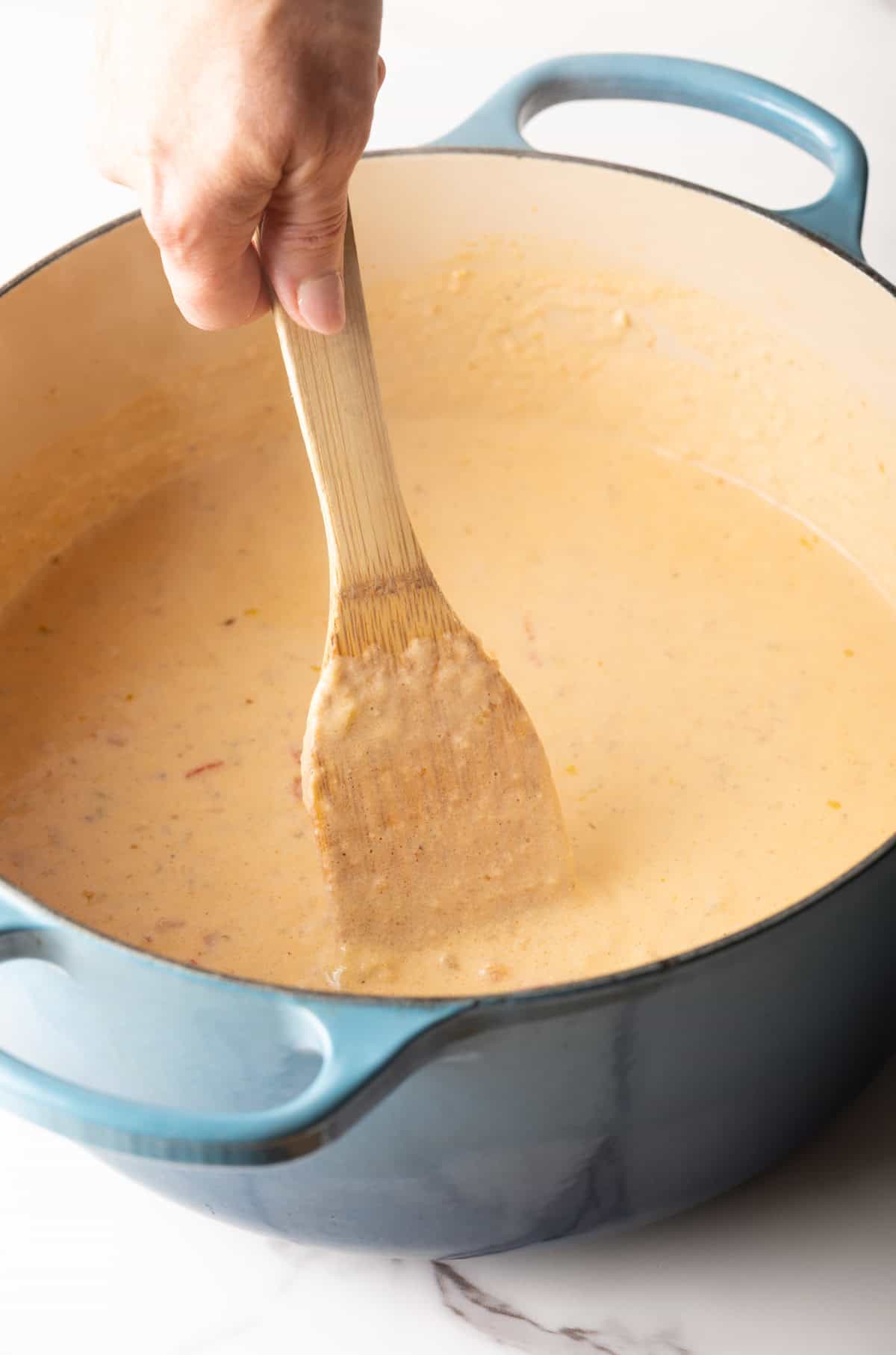 A wooden spoon is stirring the milk and roux mixture in a pot.