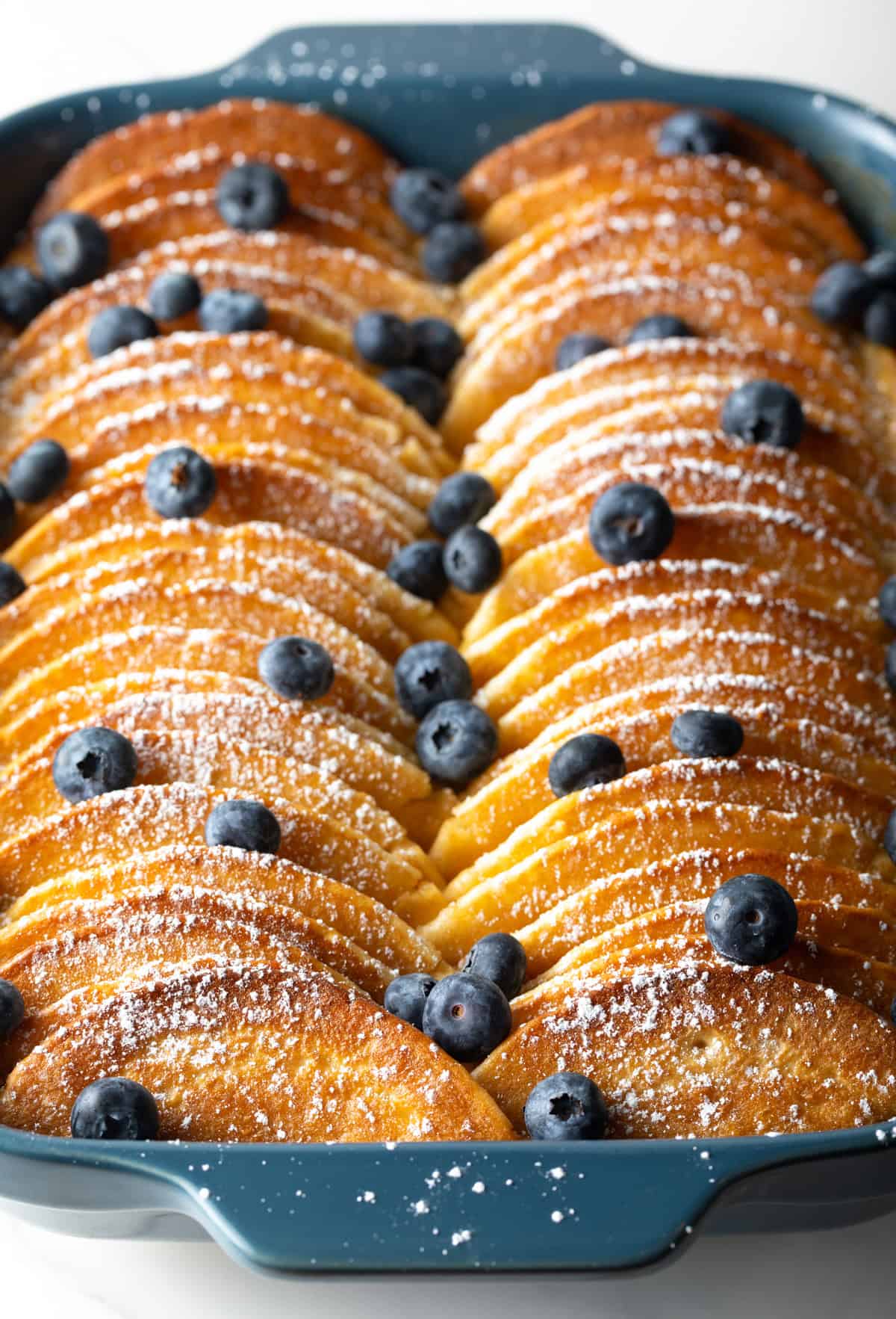 Blueberry-topped pancakes lined up in a blue casserole dish for a make-ahead pancake casserole recipe.