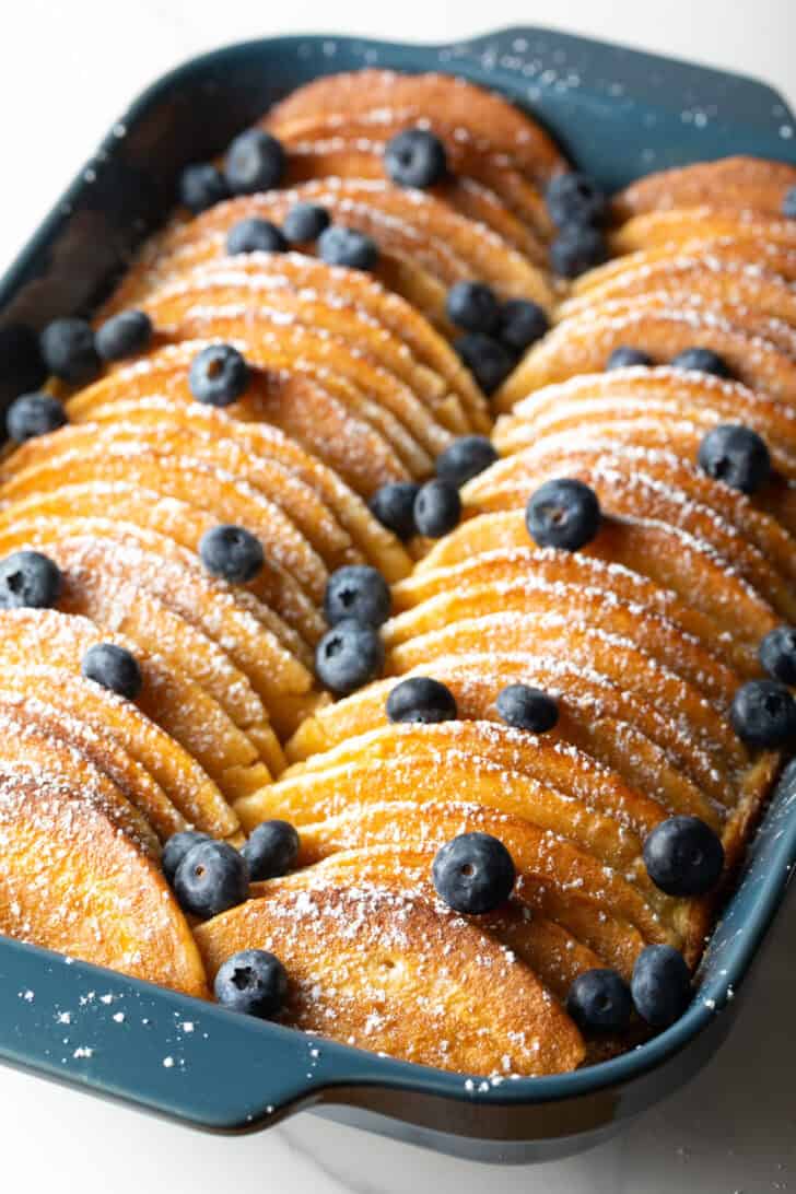 Pancakes lined up in a blue casserole dish for a make-ahead pancake breakfast casserole.