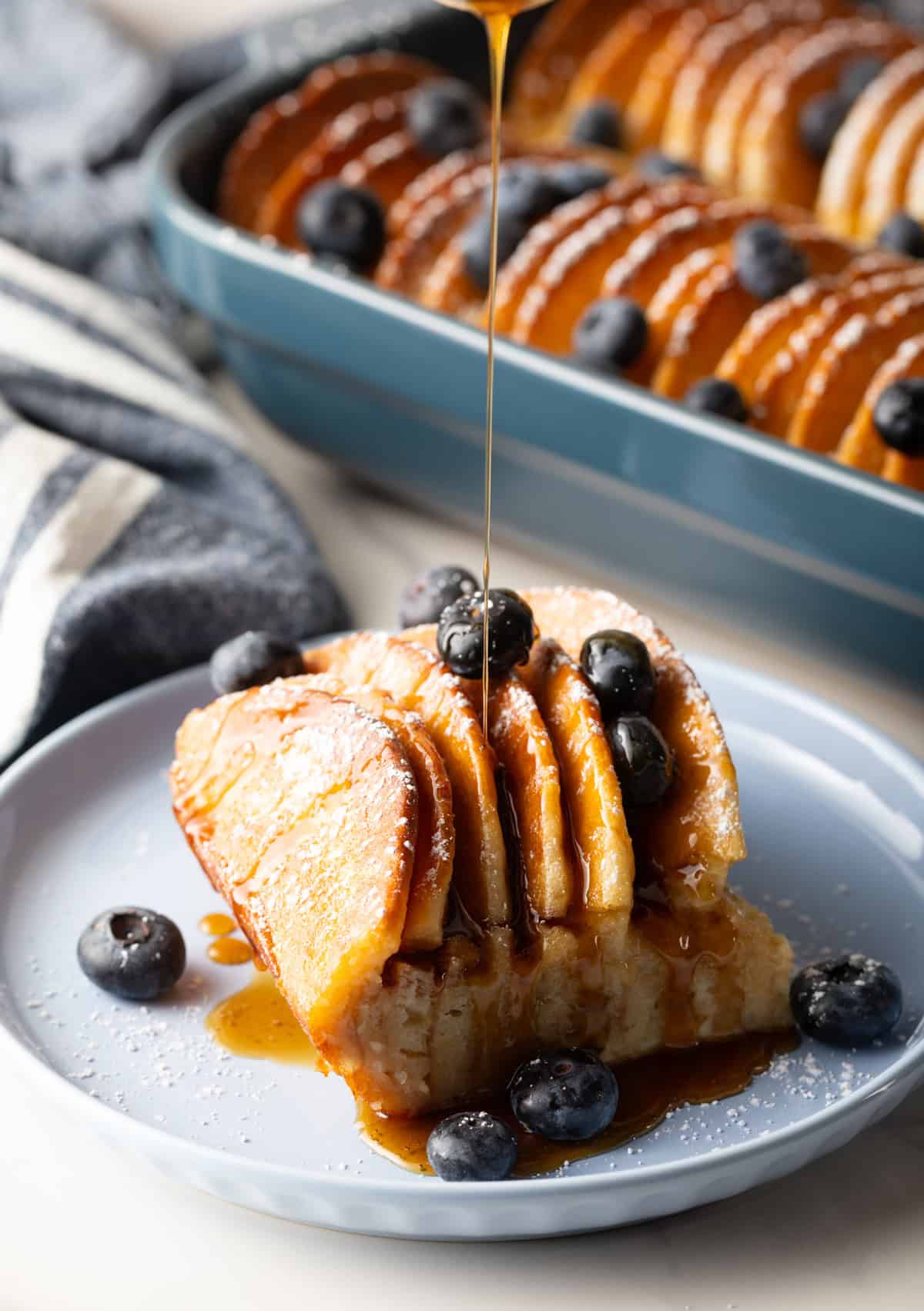 A slice of pancake casserole on a plate topped with blueberries and a drizzle of syrup.