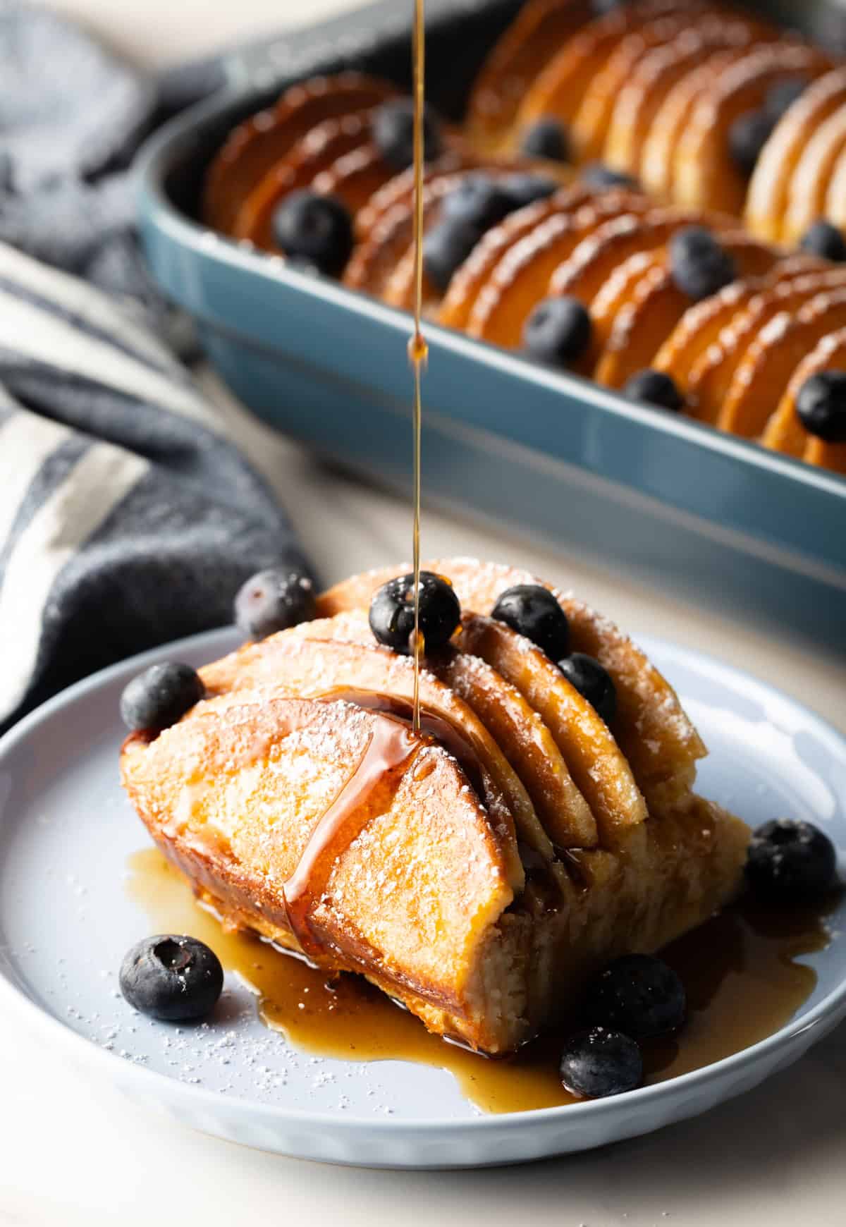 A slice of pancake casserole on a plate topped with blueberries and a drizzle of syrup.