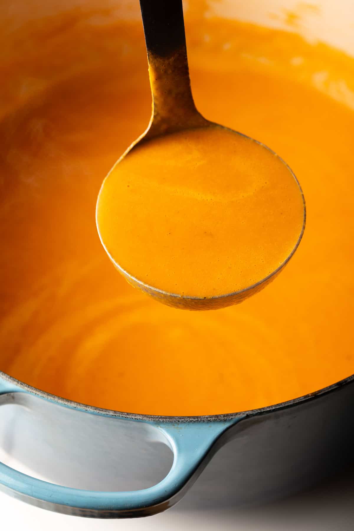 Ladleful of creamy roasted red pepper soup held to camera.