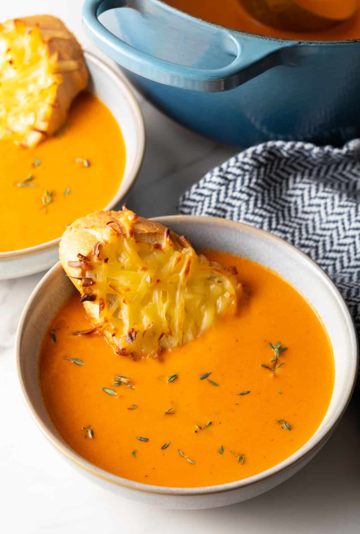 A bowl of red pepper gouda soup with a cheesy baguette slice sitting in the bowl.