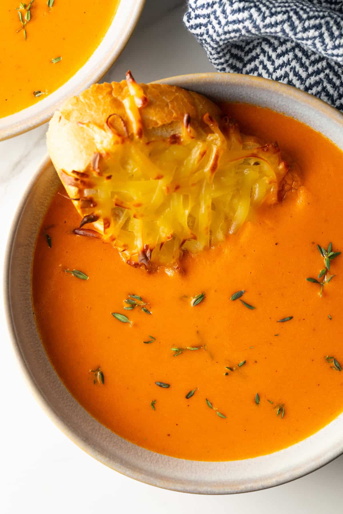 A bowl of red pepper gouda soup with a cheesy baguette slice sitting in the bowl.