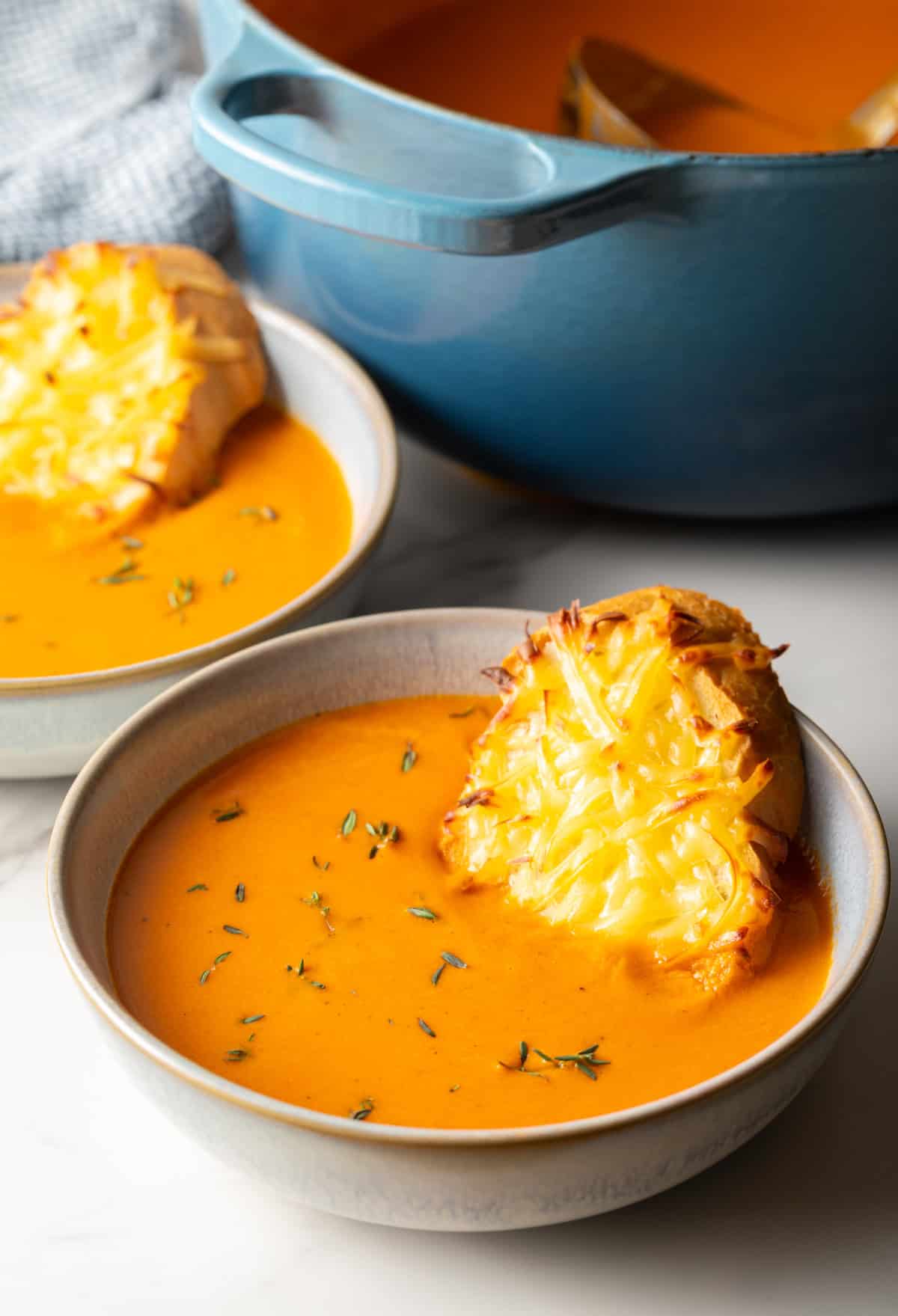 A bowl of roasted red pepper gouda soup with a cheesy baguette slice sitting in the bowl.