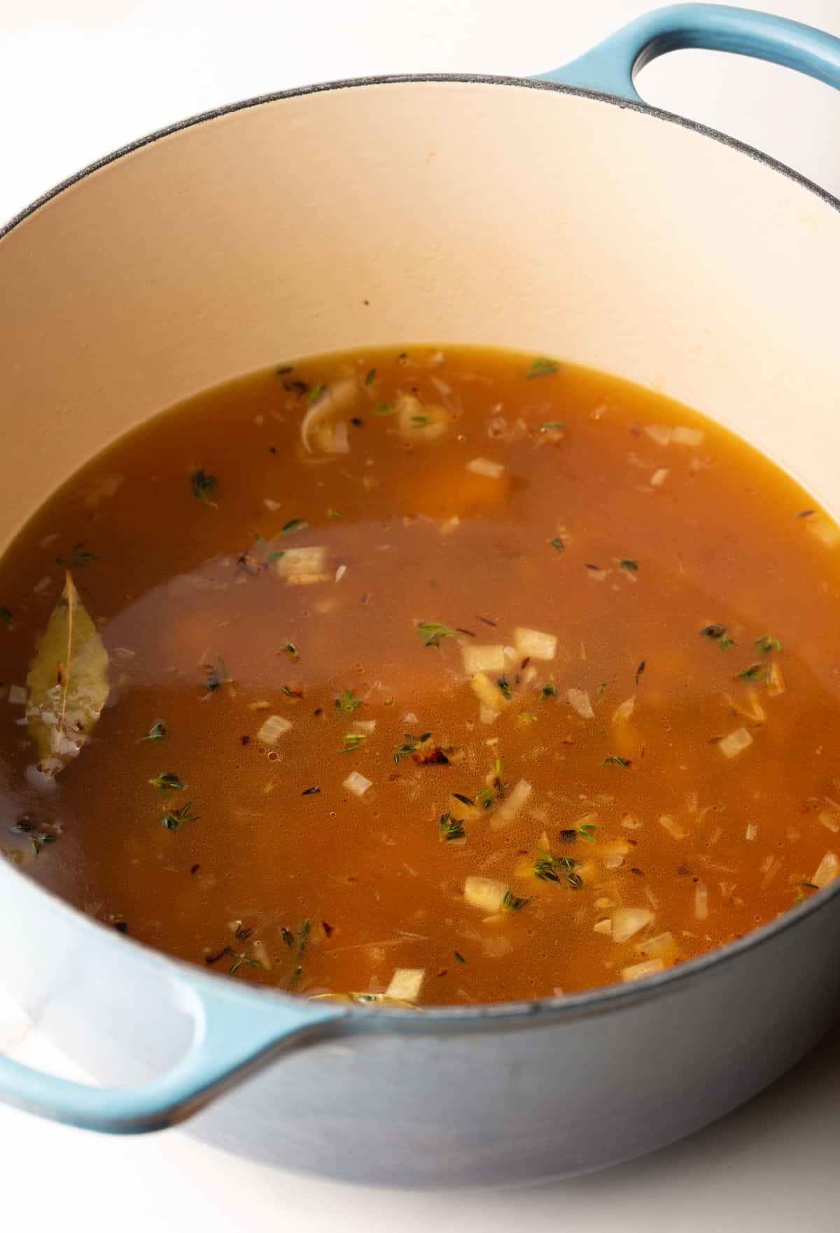 Veggies, broth, and herbs in a pot of what will become roasted red pepper gouda soup.