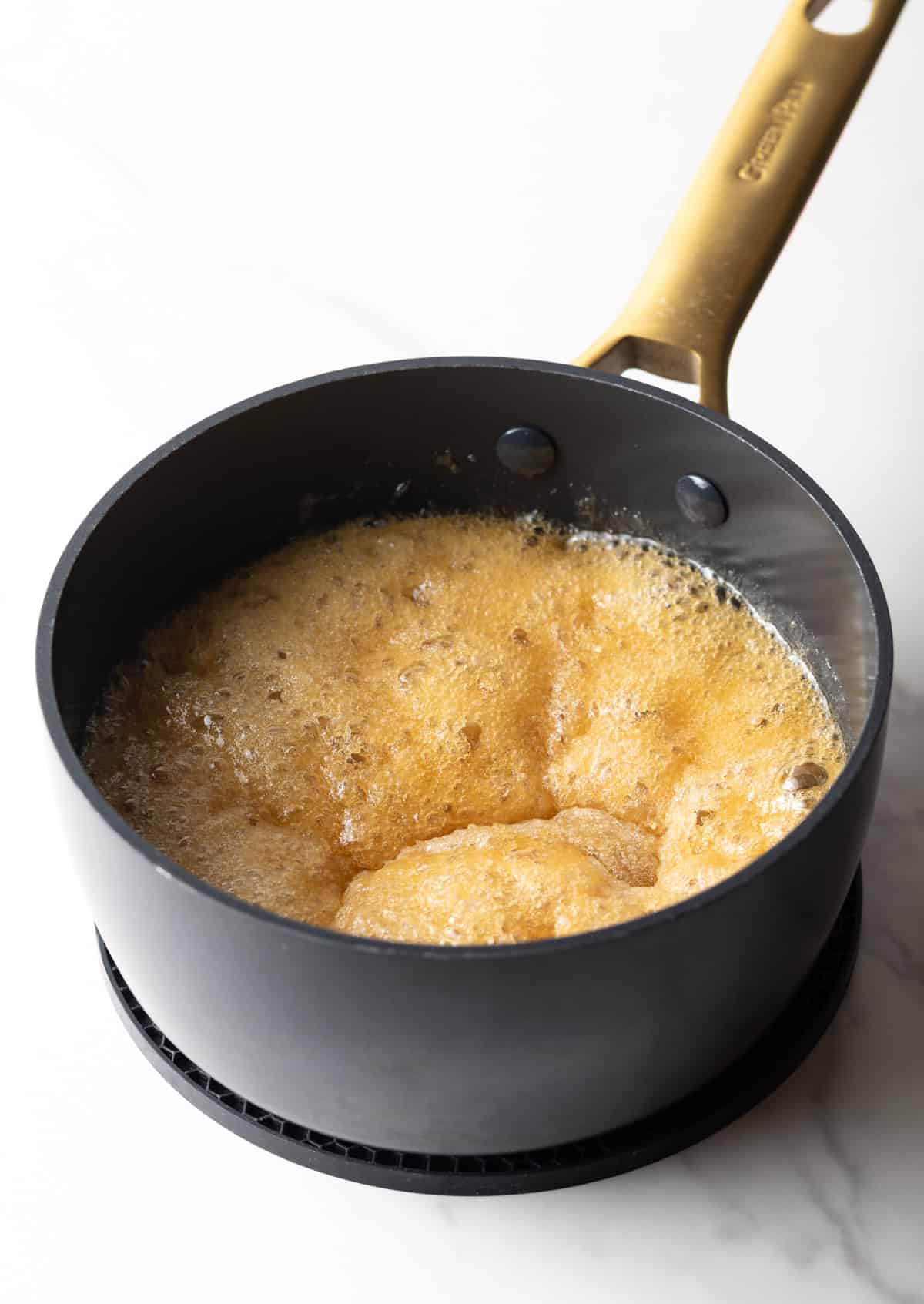A mixture of sugar and water bubbling in a black pan.