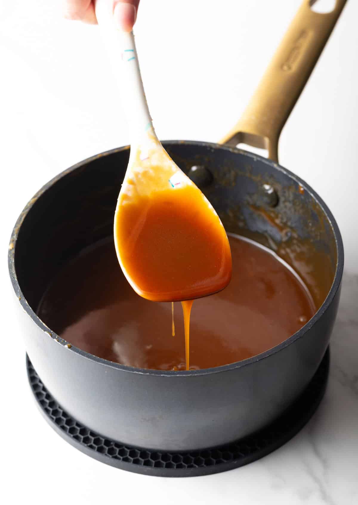 A white spatula holding salted caramel sauce over a black saucepan.