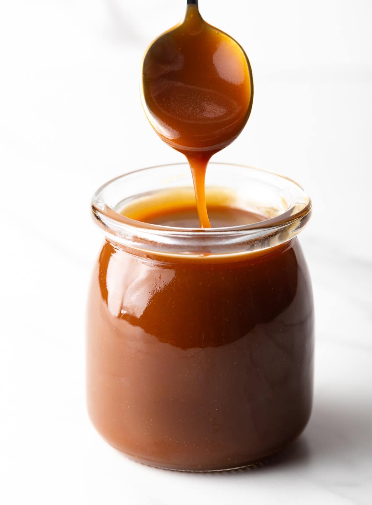 Homemade salted caramel sauce being drizzled with a spoon into a glass jar.