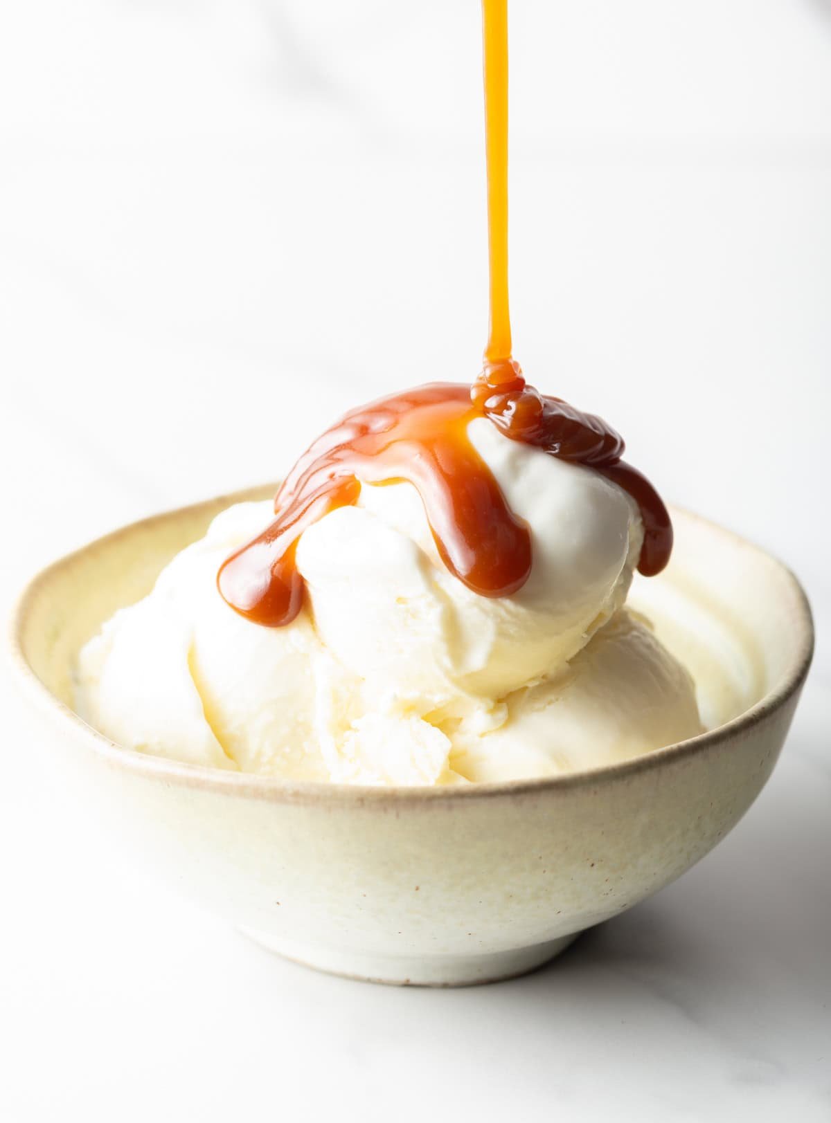 Salted caramel being drizzled over vanilla ice cream in a white bowl.