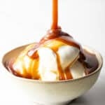Vanilla ice cream topped with rich salted caramel sauce in a rustic bowl on a white background.