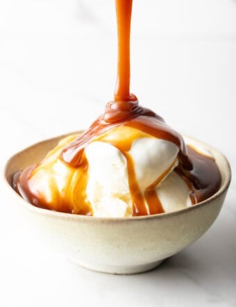 Vanilla ice cream topped with rich salted caramel sauce in a rustic bowl on a white background.