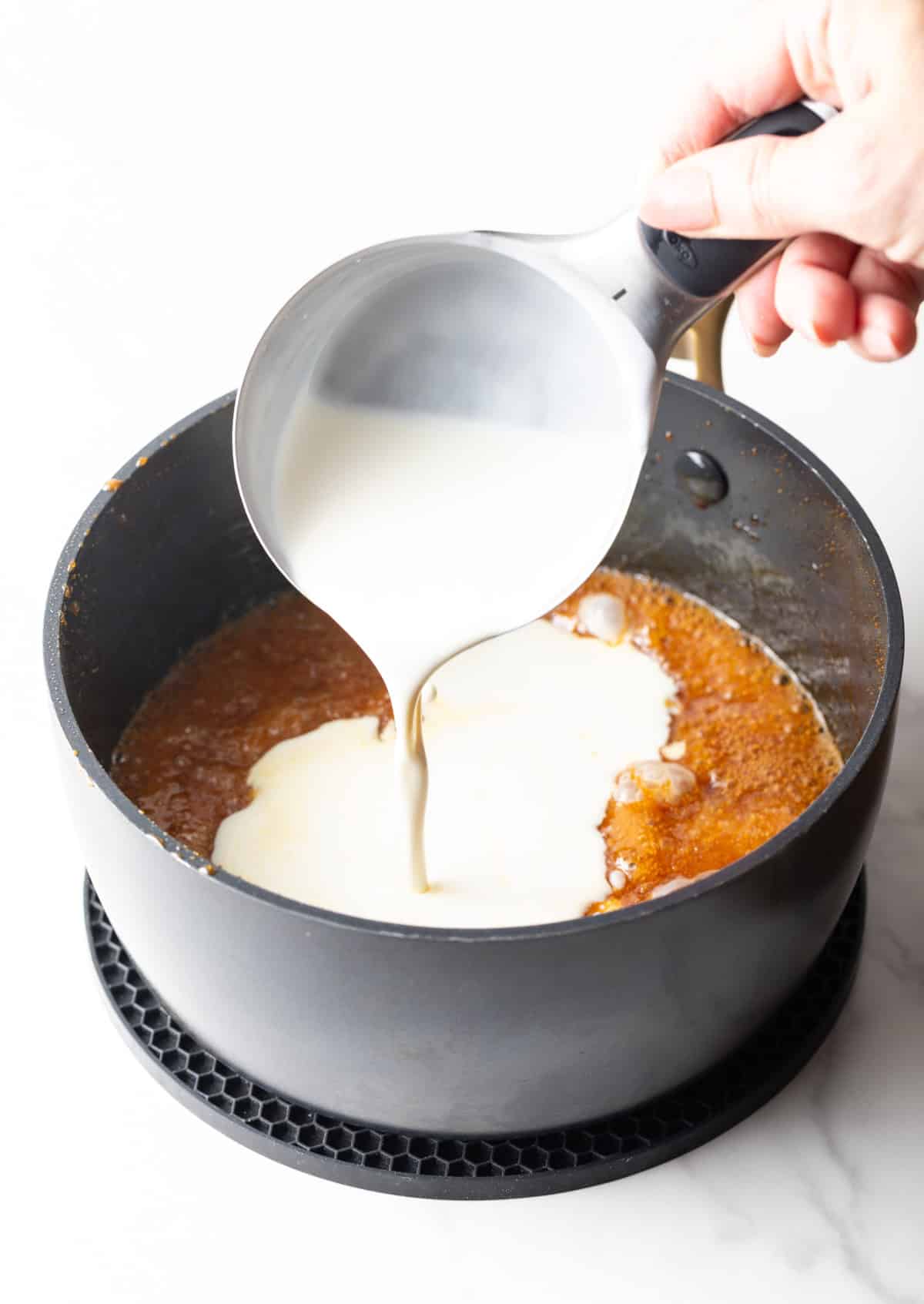 Cream being added to salted caramel sauce mixture in a black sauce pot.