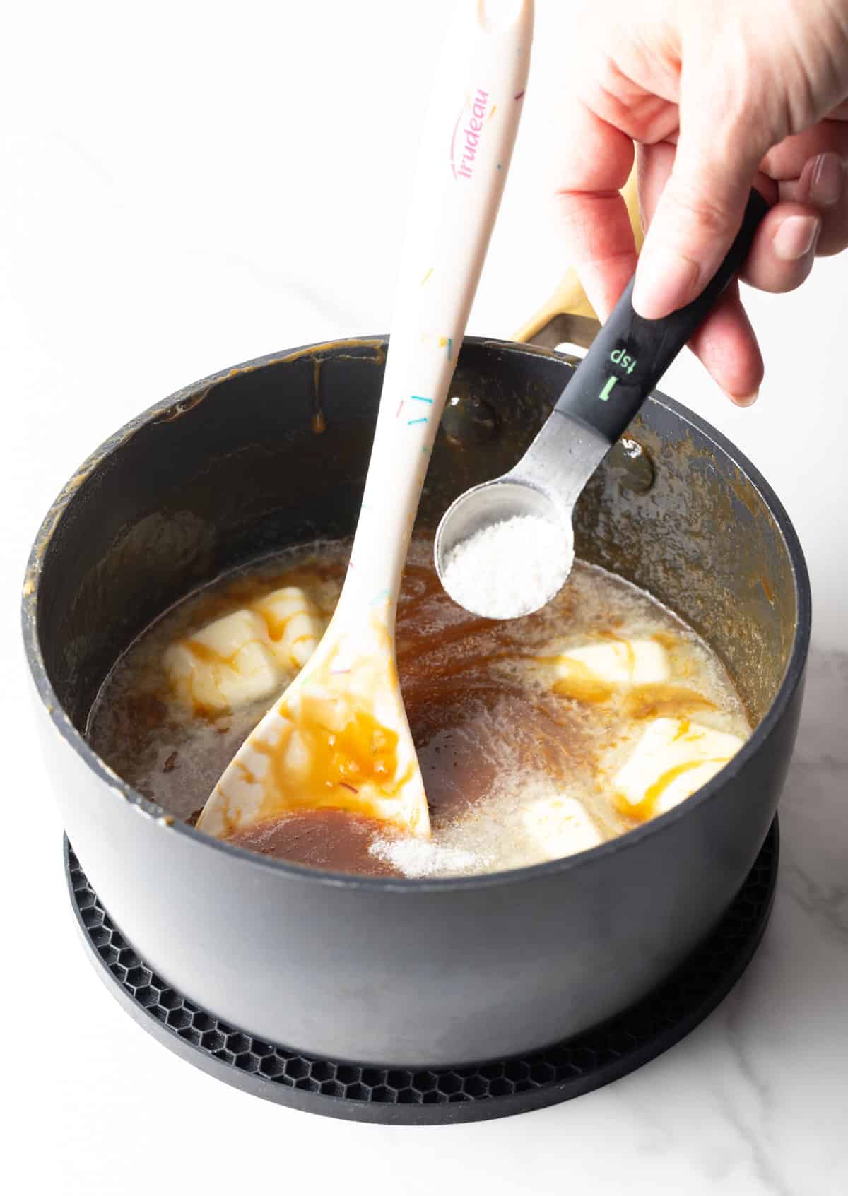 Ingredients being added to salted caramel sauce in a black sauce pan.