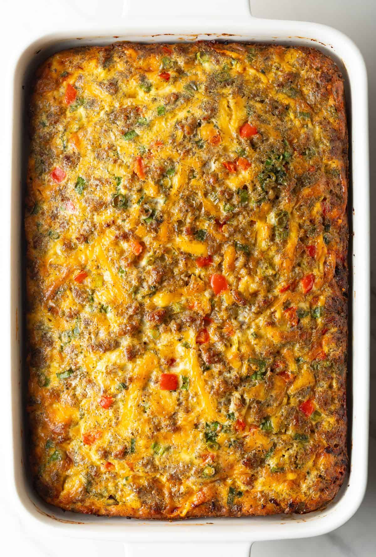 Top down view baked egg sausage and cheese casserole in a white rectangle dish.