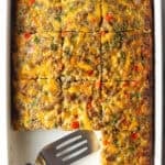 Pan of egg casserole with sausage and vegges. A spatula is in the pan, with square portions of the casserole removed.