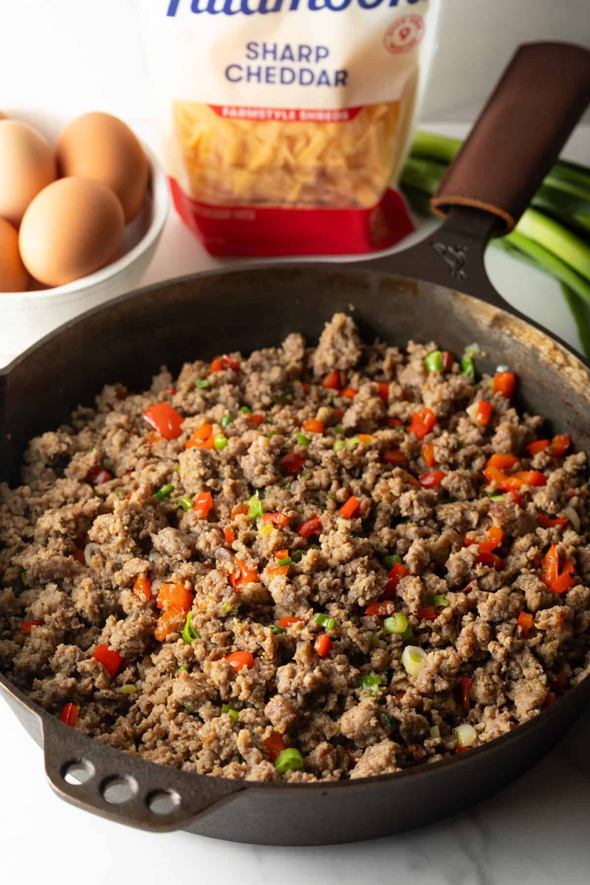 Cooking ground sausage in a cast iron skillet with diced red peppers.