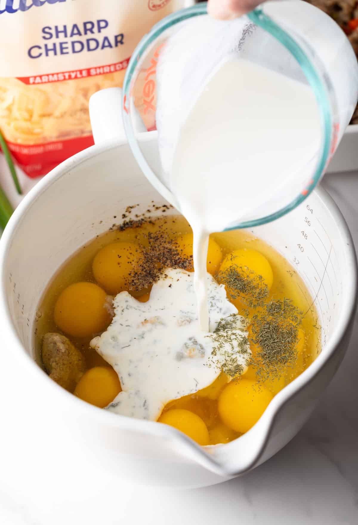 Adding milk to raw eggs in a white measuring pitcher.