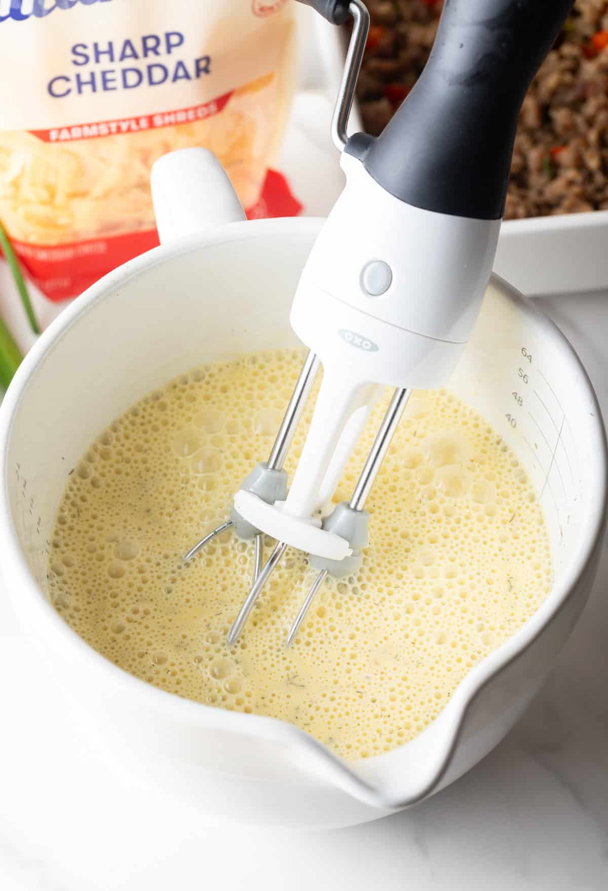 Hand mixer blending eggs and spices in a white measuring pitcher.