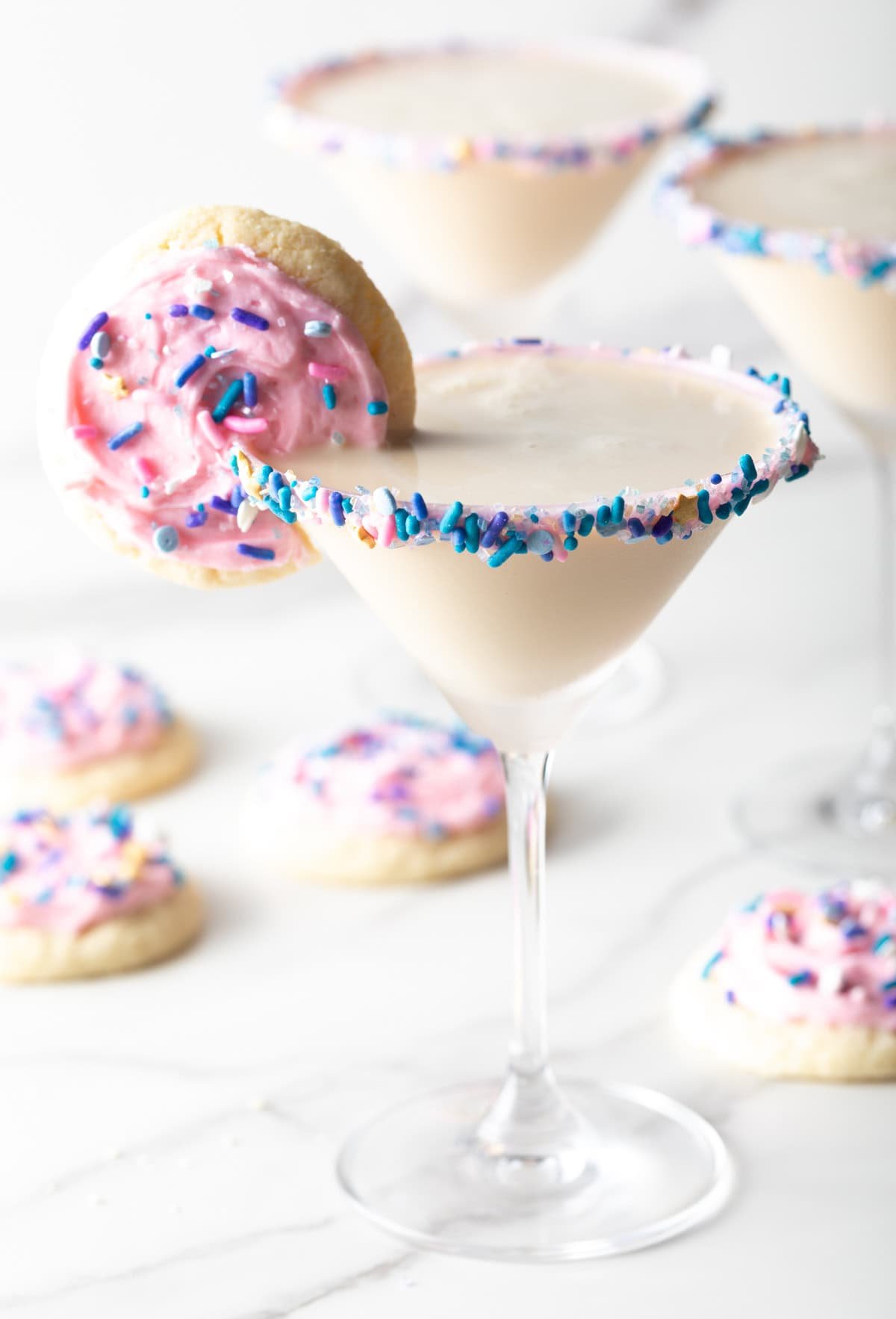Finished sugar cookie martini surrounded by iced sugar cookies with a sugar cookie on the rim.