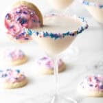 Colorful sugar cookie martini with a cookie on the rim surrounded by iced sugar cookies.