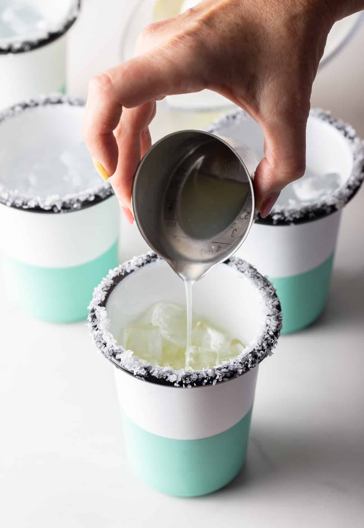 Hand pouring liquid from a metal shot glass into a cup with a salted rim.