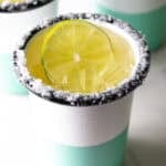 White and green-striped cup with salt around the rim and slice of lime in the drink.