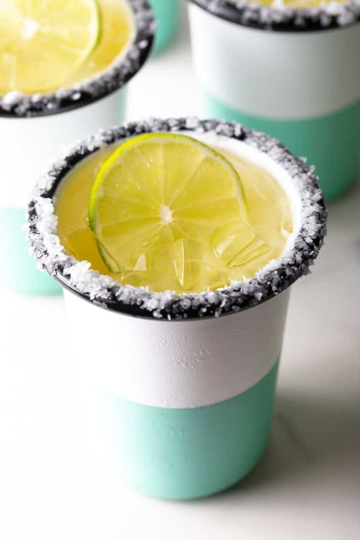White and green-striped cup with salt around the rim and slice of lime in the drink.