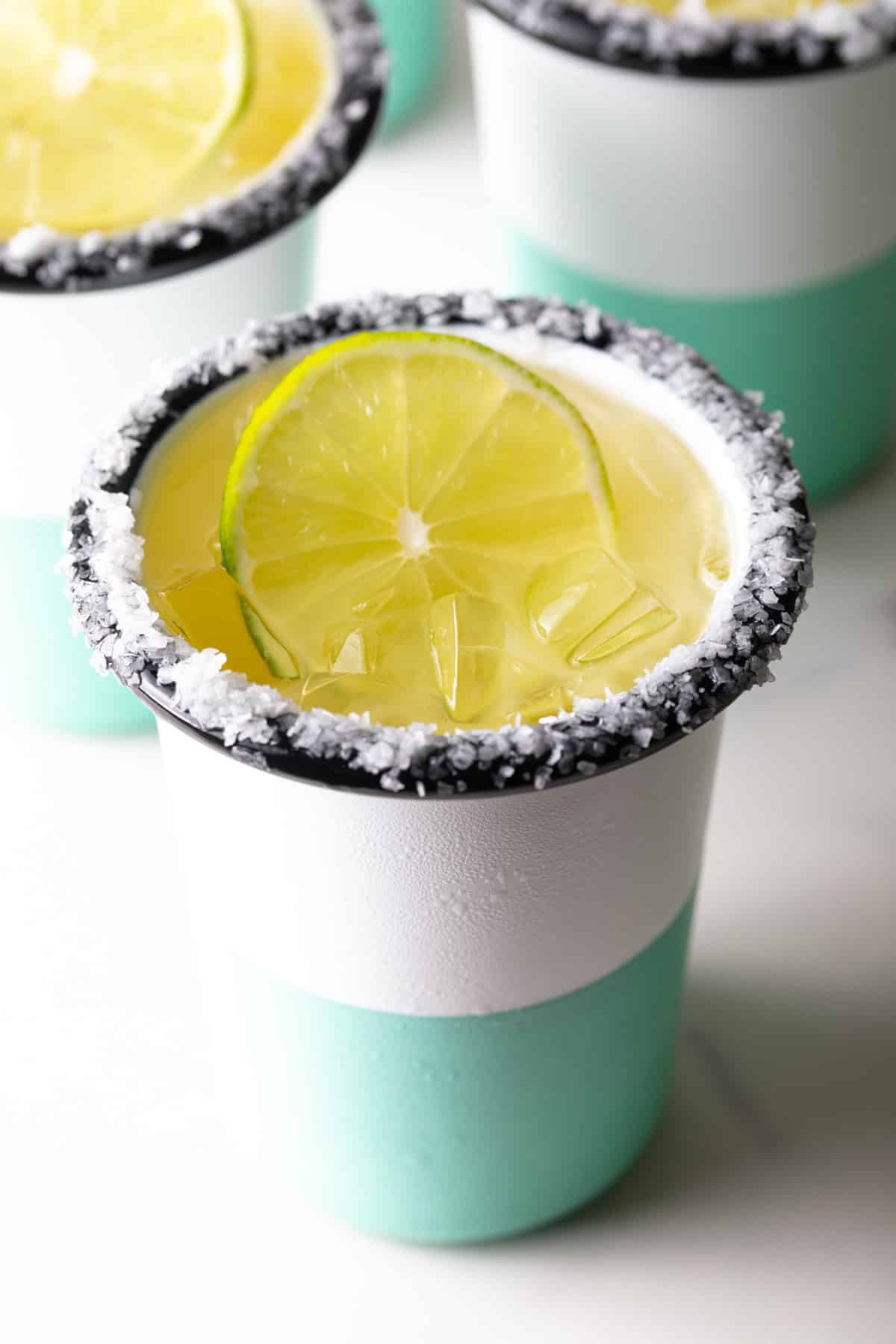 White and green-striped cup with salt around the rim and slice of lime in the drink.