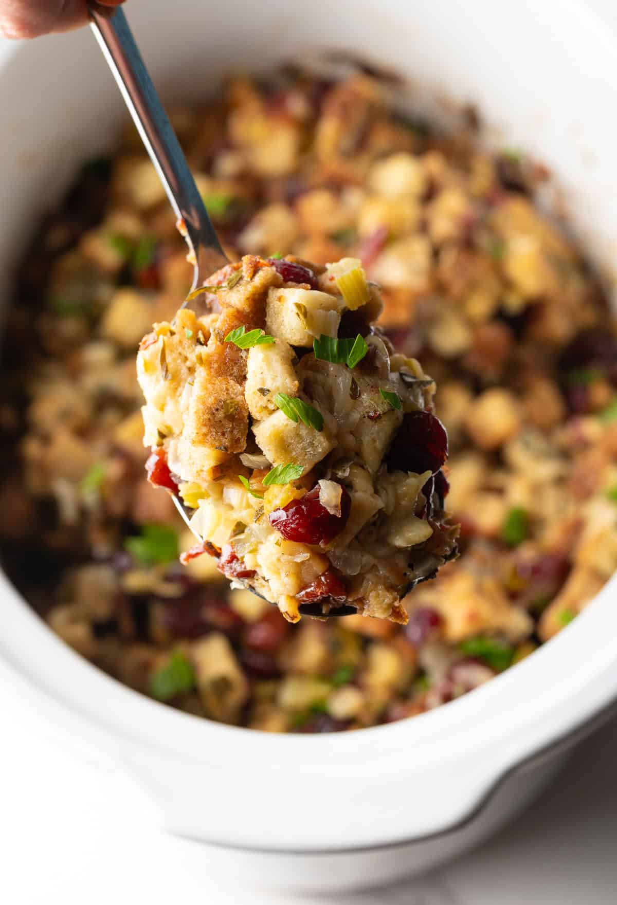 crock pot stuffing lifted on serving spoon over white slow cooker