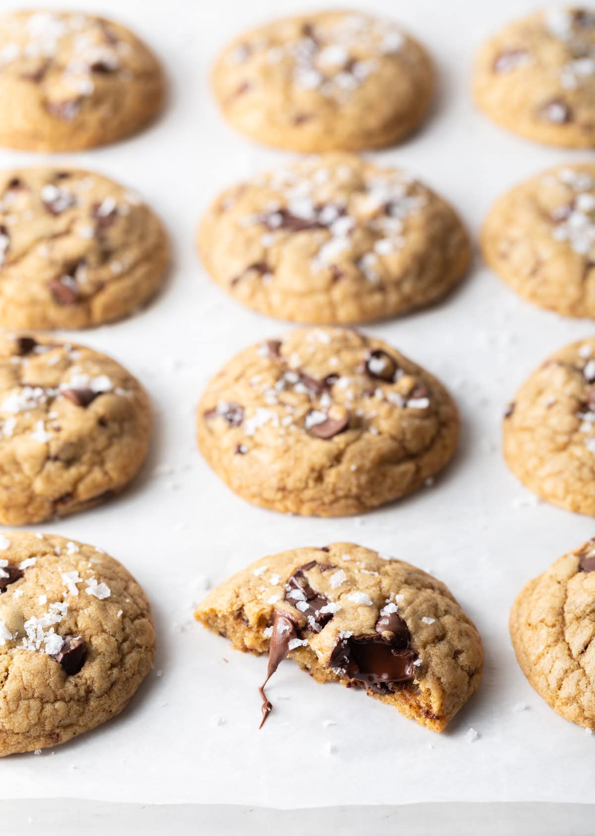 Top down chocolate chip cookies on a baking sheet. One cookie in the front has been broken in half.