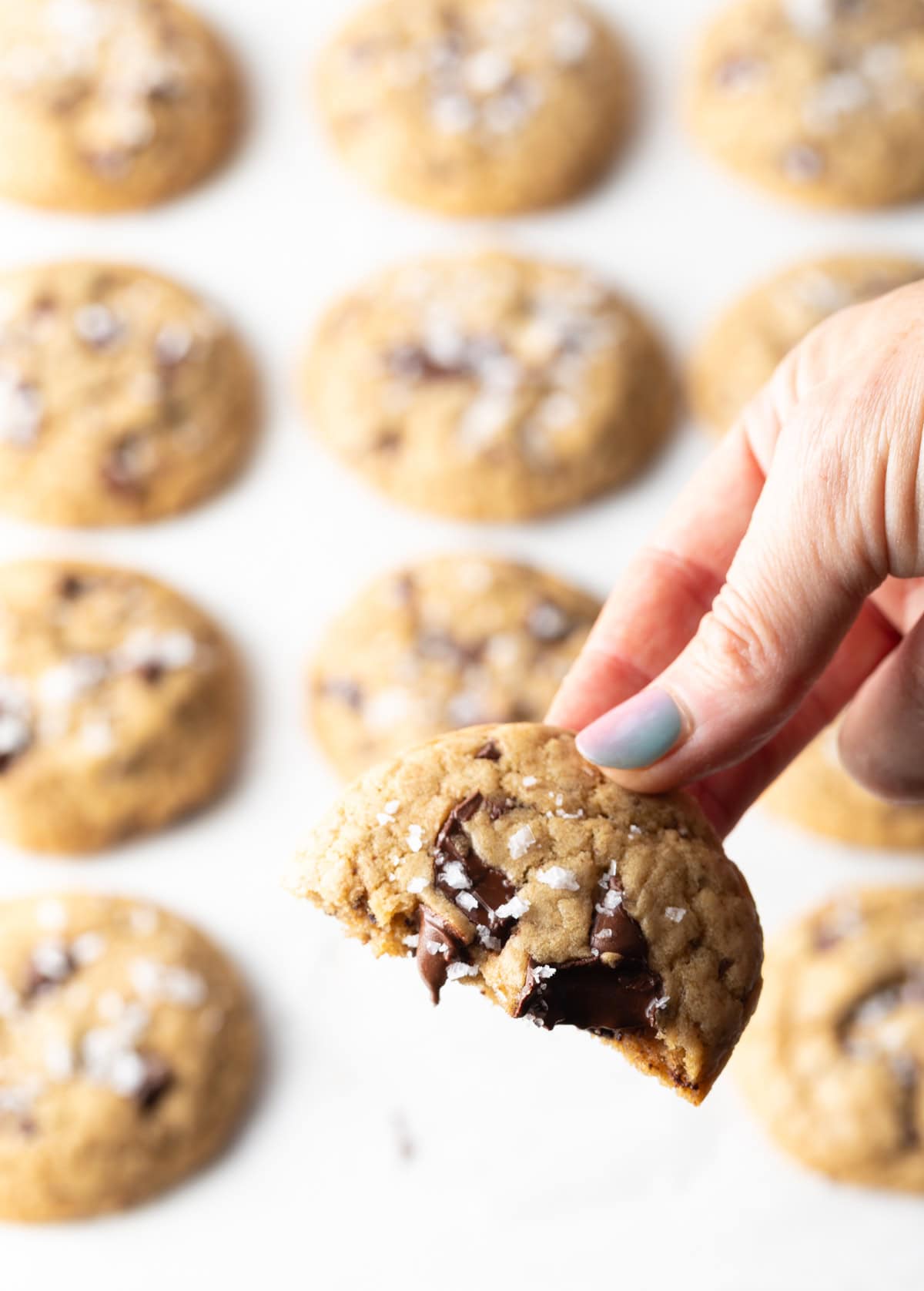 Hand holding half of a brown sugar chocolate chip cookie to camera.