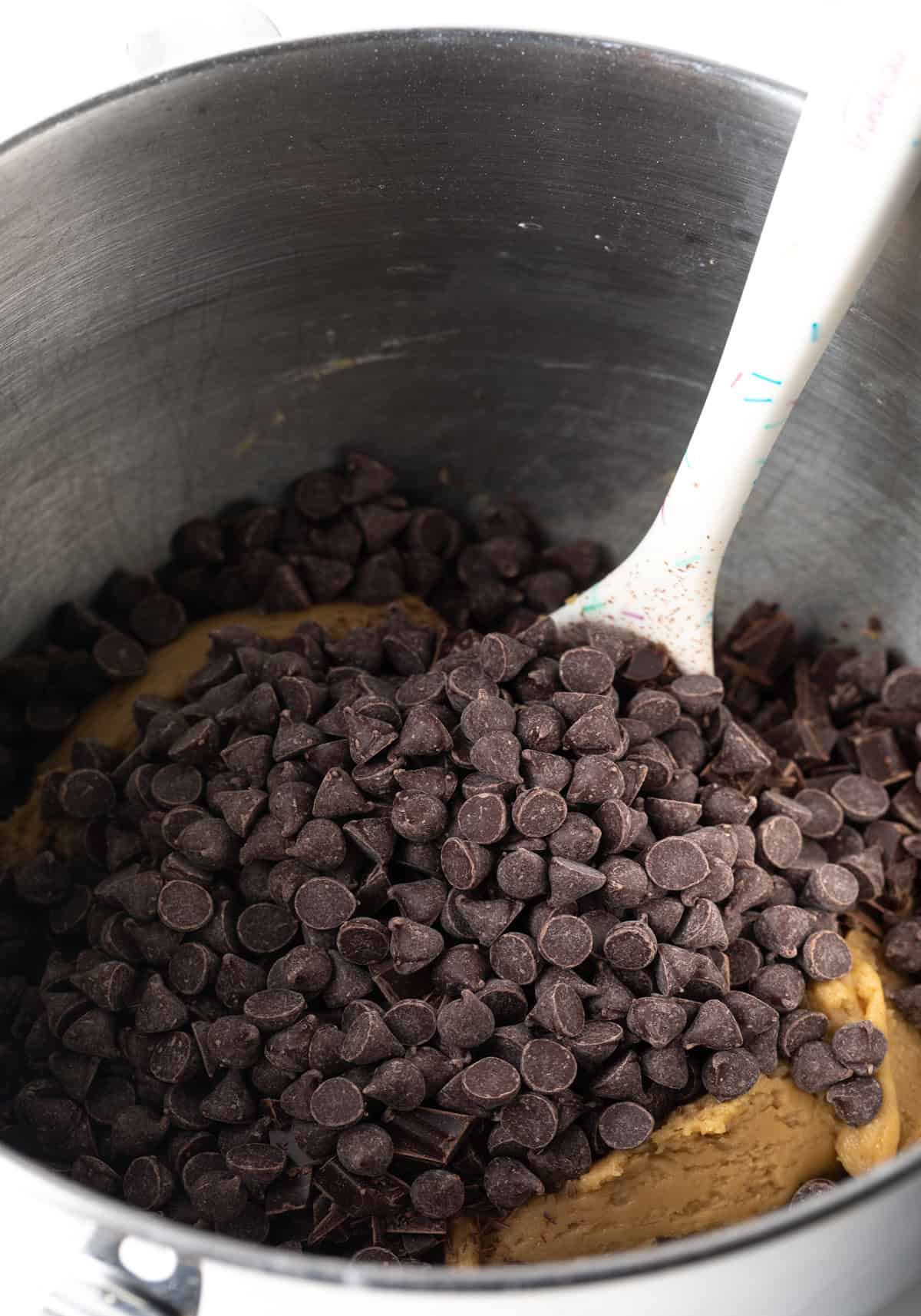 Chocolate chips added to the metal mixing bowl with cookie dough.