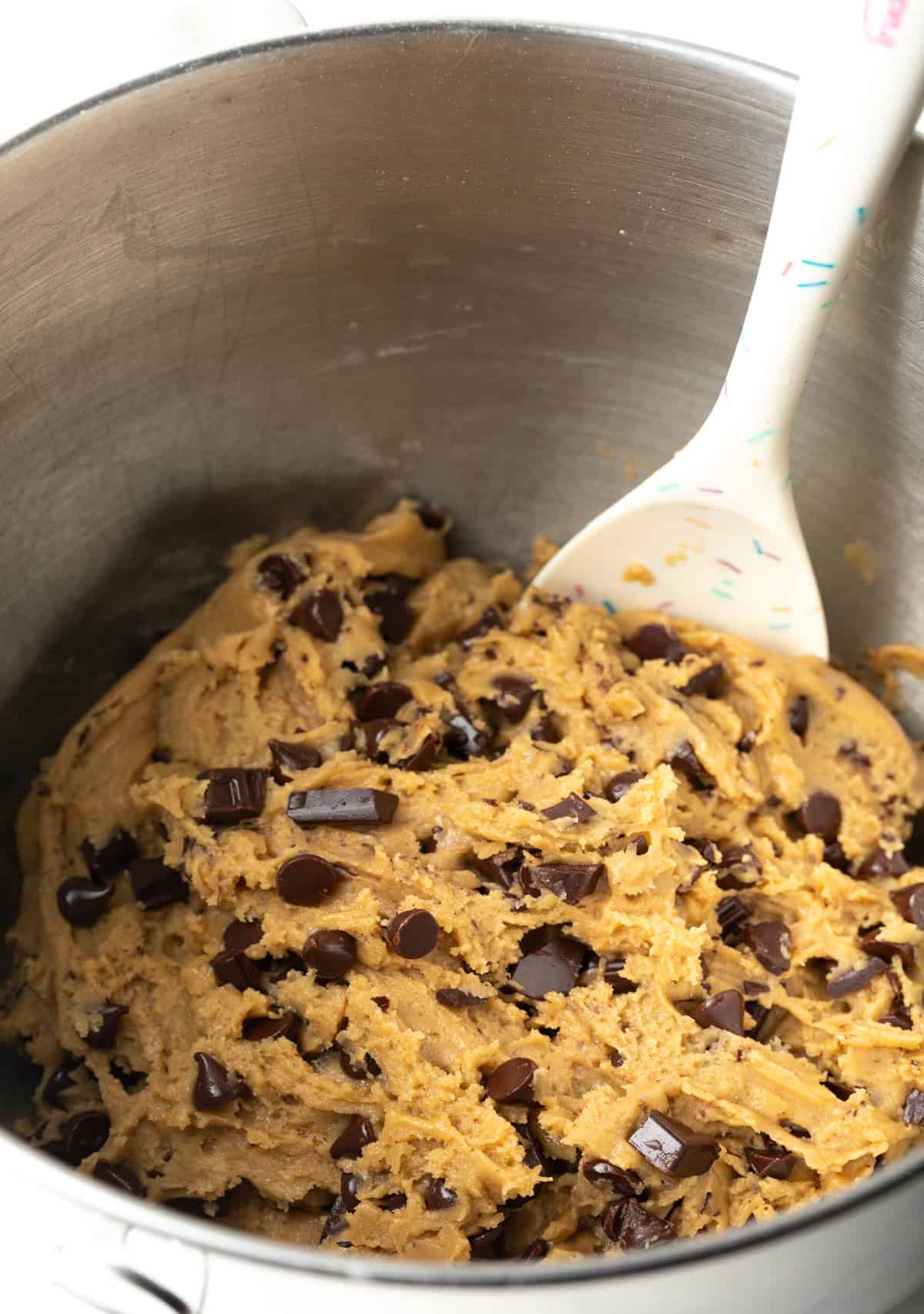 Using a spatula to stir chocolate chunks into brown sugar cookie dough.